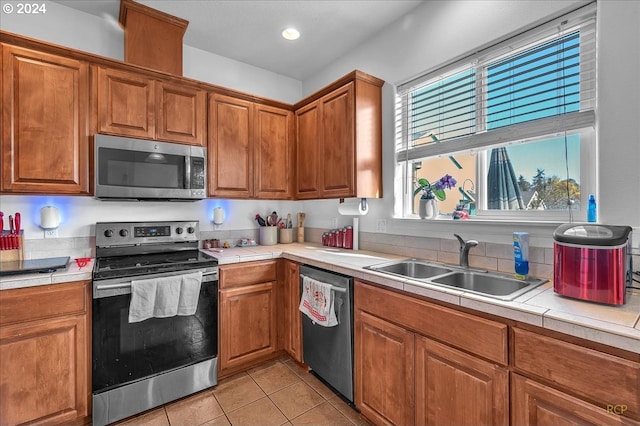 kitchen with appliances with stainless steel finishes, tile countertops, sink, and plenty of natural light