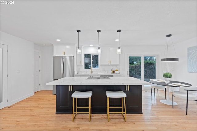 kitchen featuring stainless steel refrigerator, light stone countertops, light hardwood / wood-style flooring, a spacious island, and white cabinets