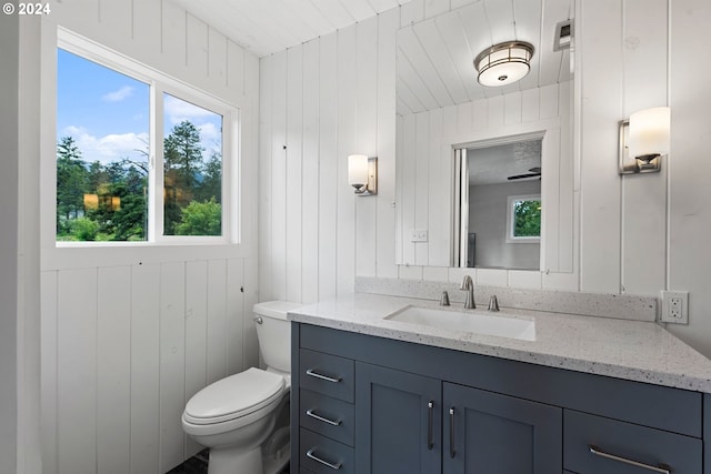 bathroom with vanity, toilet, a healthy amount of sunlight, and wood walls