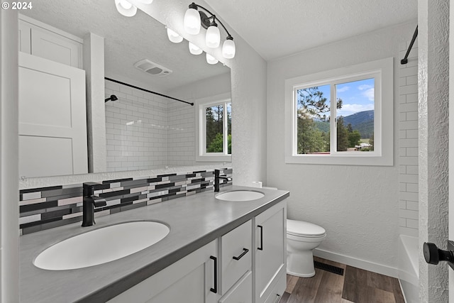 full bathroom featuring decorative backsplash, wood-type flooring, a textured ceiling, and vanity