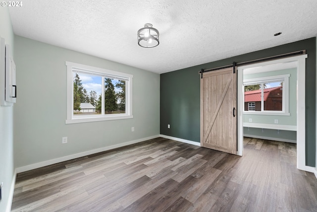 unfurnished bedroom with a barn door, a textured ceiling, and hardwood / wood-style flooring