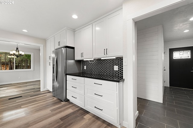 kitchen with dark wood-type flooring, an inviting chandelier, white cabinets, stainless steel refrigerator with ice dispenser, and decorative backsplash