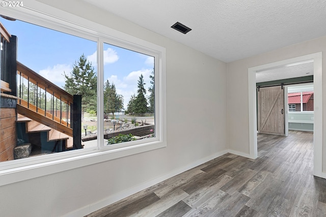 unfurnished room featuring a barn door, wood-type flooring, a textured ceiling, and a wealth of natural light