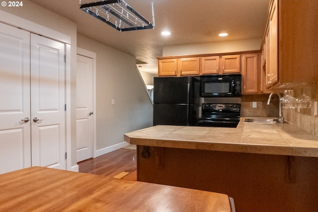 kitchen featuring decorative backsplash, light hardwood / wood-style flooring, sink, tile countertops, and black appliances