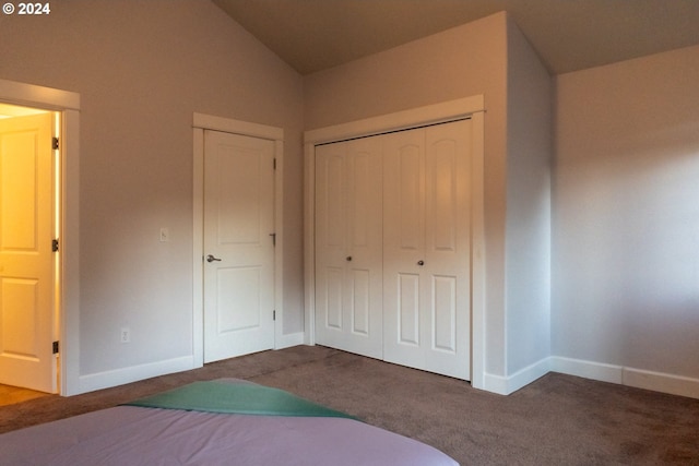 unfurnished bedroom with lofted ceiling, a closet, and dark carpet