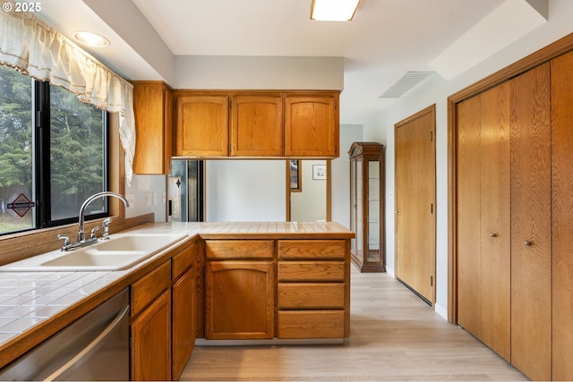 kitchen with tile countertops, dishwasher, sink, kitchen peninsula, and light wood-type flooring