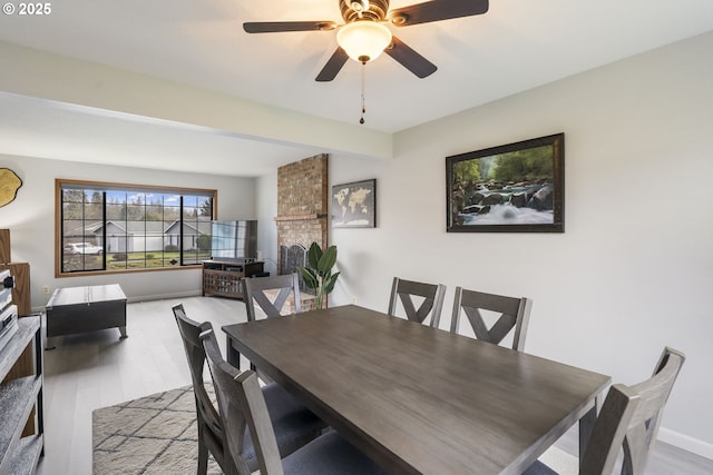 dining room with ceiling fan, a fireplace, and light hardwood / wood-style floors