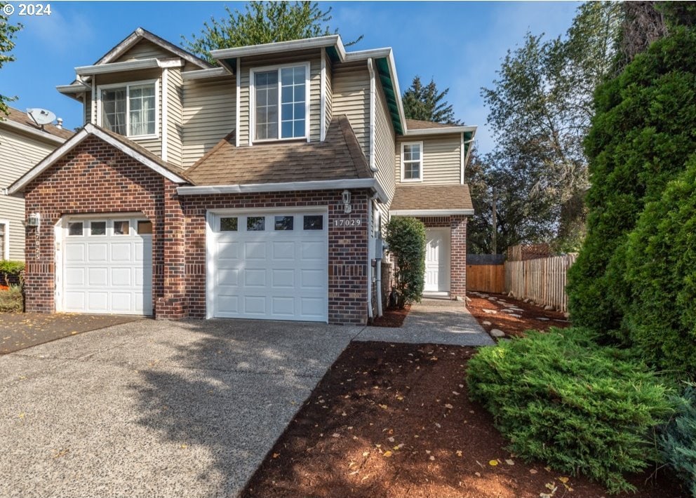 view of front facade featuring an attached garage, brick siding, fence, driveway, and roof with shingles