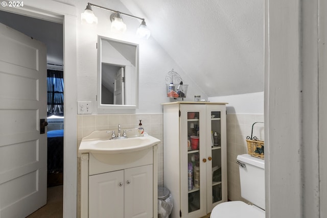 bathroom featuring vanity, toilet, tile walls, and vaulted ceiling