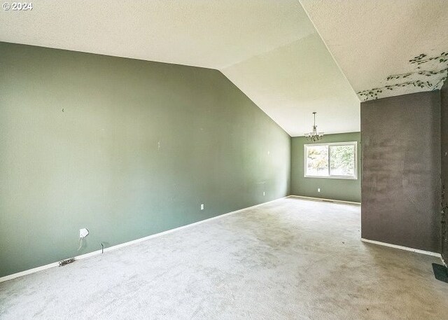 carpeted empty room with an inviting chandelier, vaulted ceiling, and a textured ceiling