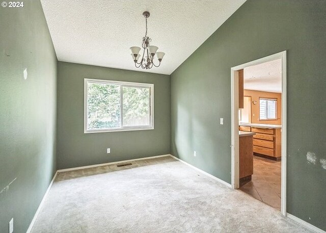 carpeted empty room with a textured ceiling, an inviting chandelier, and lofted ceiling