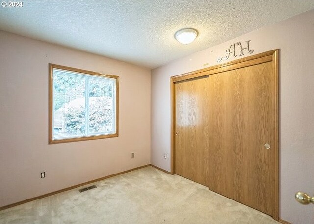 unfurnished bedroom featuring a textured ceiling, light carpet, and a closet