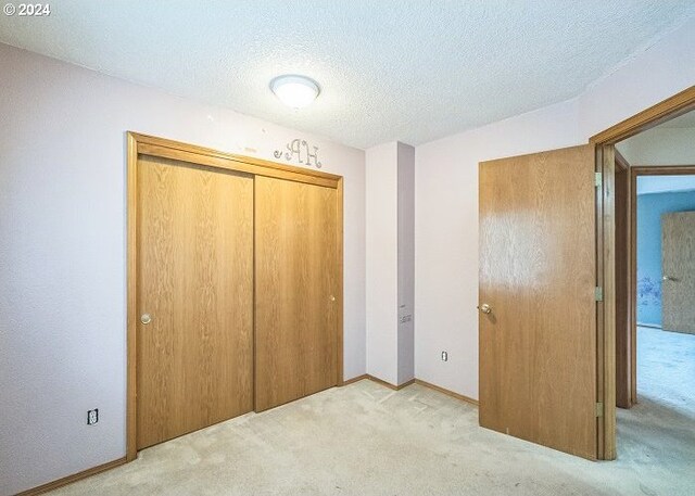 unfurnished bedroom with a textured ceiling, light carpet, and a closet