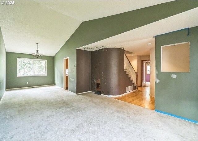 carpeted empty room featuring vaulted ceiling and a notable chandelier