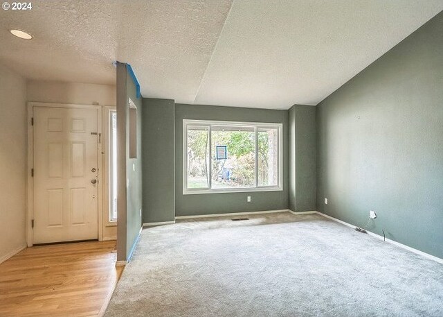 entryway featuring a textured ceiling, light wood-type flooring, and vaulted ceiling