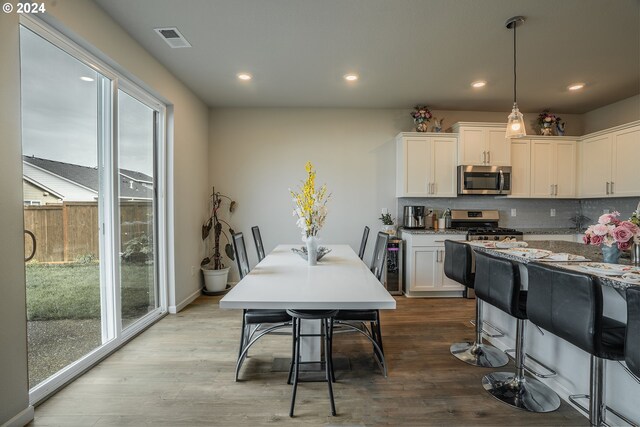 kitchen with decorative backsplash, pendant lighting, light hardwood / wood-style flooring, stainless steel appliances, and white cabinetry