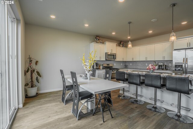 kitchen featuring decorative light fixtures, stainless steel appliances, light hardwood / wood-style floors, and decorative backsplash