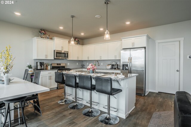 kitchen with pendant lighting, an island with sink, dark wood-type flooring, white cabinetry, and stainless steel appliances