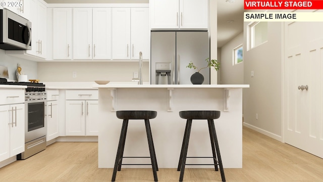 kitchen with a kitchen bar, light hardwood / wood-style floors, white cabinetry, and stainless steel appliances