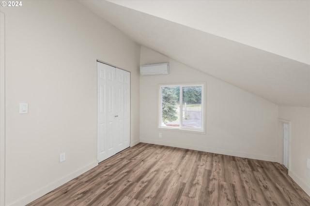 additional living space with wood-type flooring, lofted ceiling, and a wall mounted air conditioner