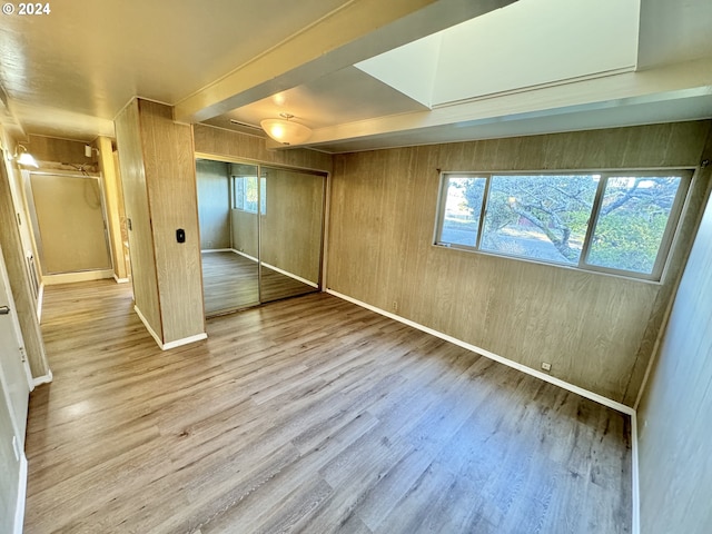 unfurnished bedroom featuring multiple windows, wood finished floors, a closet, and wood walls