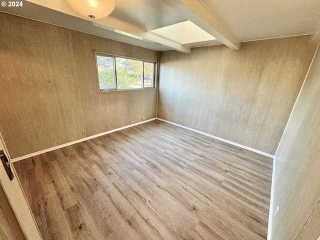 empty room featuring beamed ceiling, wood walls, and hardwood / wood-style flooring