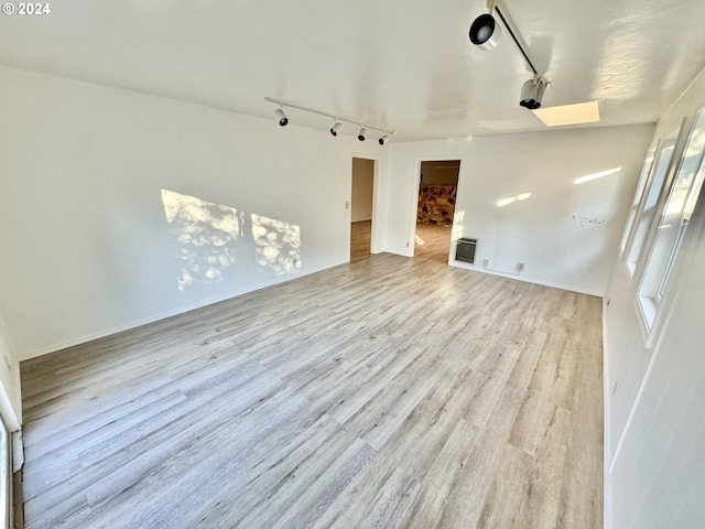 unfurnished living room featuring track lighting, wood finished floors, and baseboards