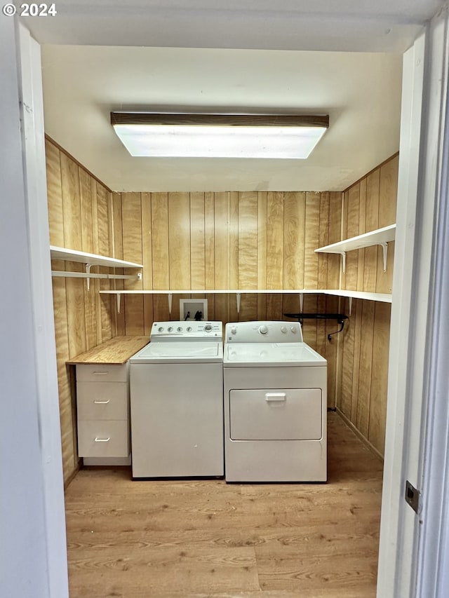 laundry room with washing machine and clothes dryer, light wood-style flooring, and wooden walls