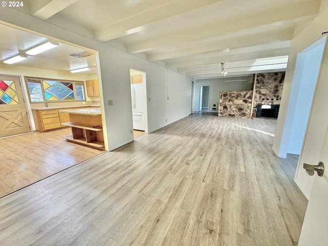 unfurnished living room featuring beam ceiling, built in desk, and light hardwood / wood-style flooring