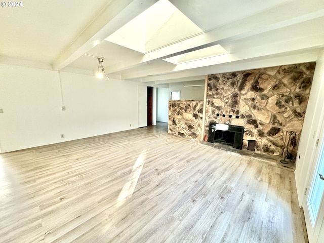 unfurnished living room featuring wood-type flooring, beam ceiling, a stone fireplace, and a skylight