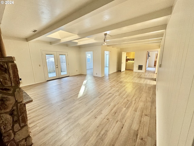 unfurnished living room featuring light wood-style floors, beamed ceiling, and french doors