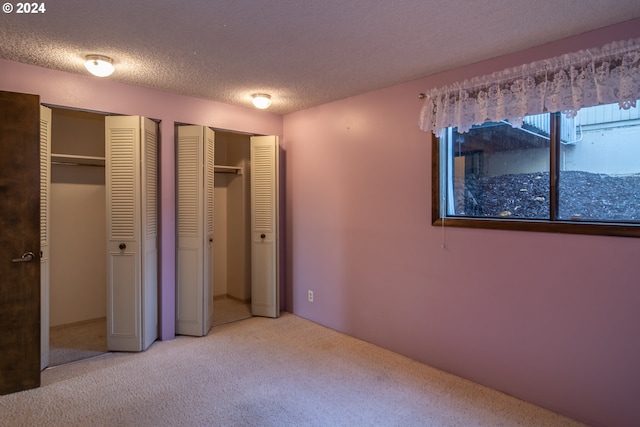 unfurnished bedroom with a textured ceiling, multiple closets, and light colored carpet