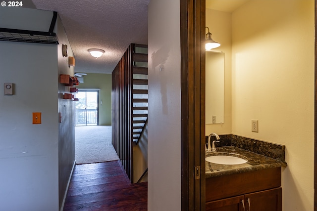 corridor with dark wood-type flooring, sink, and a textured ceiling