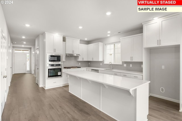 kitchen featuring under cabinet range hood, stainless steel appliances, a kitchen island, a sink, and light countertops