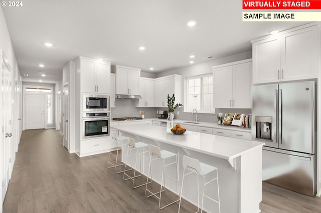 kitchen featuring under cabinet range hood, stainless steel appliances, a sink, white cabinets, and light wood-type flooring