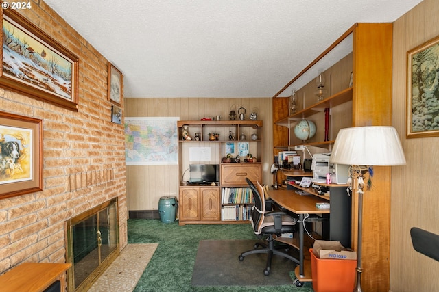 carpeted home office with a textured ceiling, a fireplace, built in desk, wood walls, and wainscoting