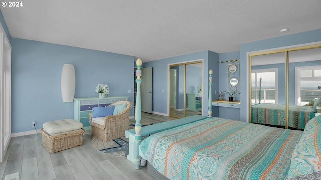 bedroom featuring light hardwood / wood-style flooring, two closets, and a textured ceiling