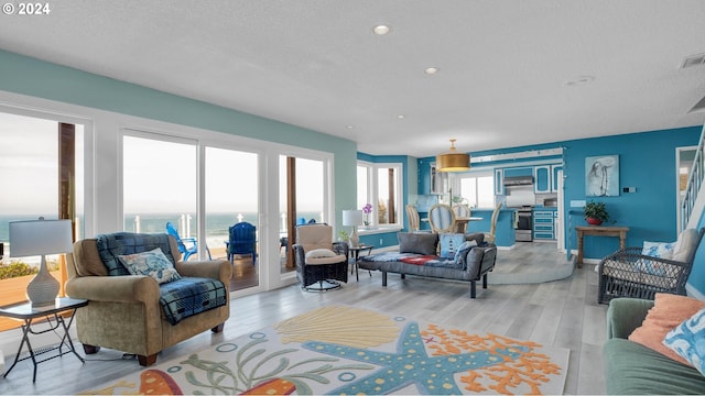 living room with a water view, light hardwood / wood-style floors, plenty of natural light, and a textured ceiling