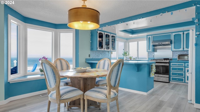 dining space featuring a textured ceiling, light hardwood / wood-style flooring, a water view, and a wealth of natural light