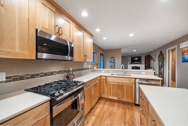 kitchen featuring sink, stainless steel appliances, kitchen peninsula, light hardwood / wood-style floors, and decorative backsplash