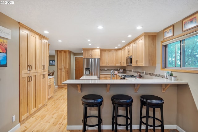 kitchen with kitchen peninsula, a kitchen breakfast bar, decorative backsplash, light brown cabinetry, and stainless steel appliances