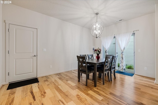 dining space featuring a notable chandelier, light wood-type flooring, and a textured ceiling