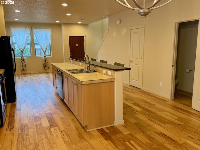 kitchen featuring black appliances, sink, light hardwood / wood-style flooring, a notable chandelier, and an island with sink