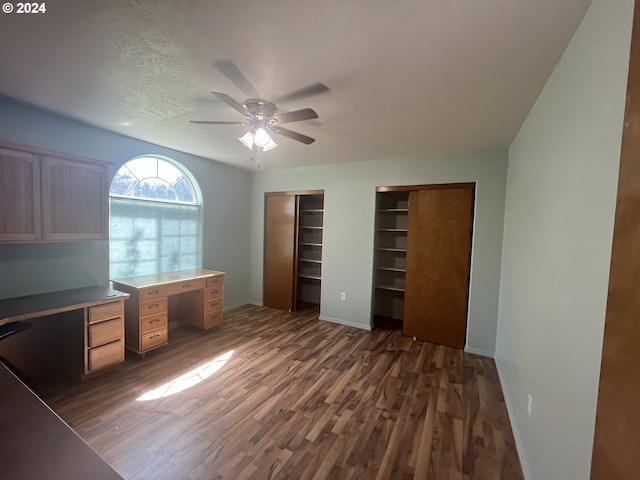 unfurnished office featuring a textured ceiling, built in desk, ceiling fan, and dark hardwood / wood-style flooring