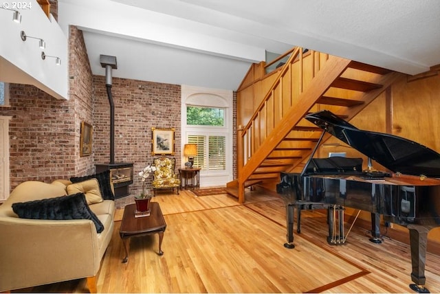 sitting room featuring a textured ceiling, a wood stove, light hardwood / wood-style flooring, lofted ceiling with beams, and brick wall