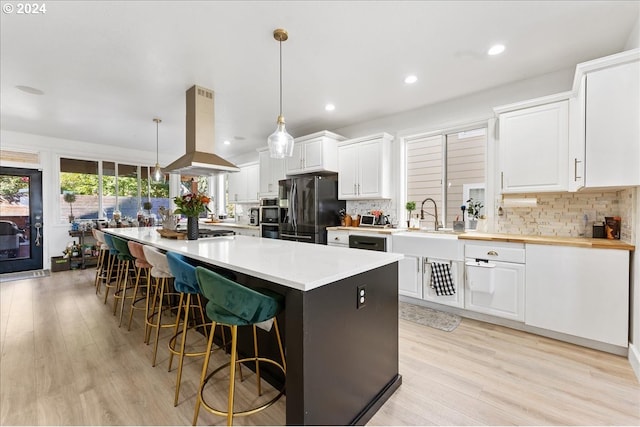 kitchen with pendant lighting, light hardwood / wood-style floors, white cabinetry, island exhaust hood, and black refrigerator with ice dispenser