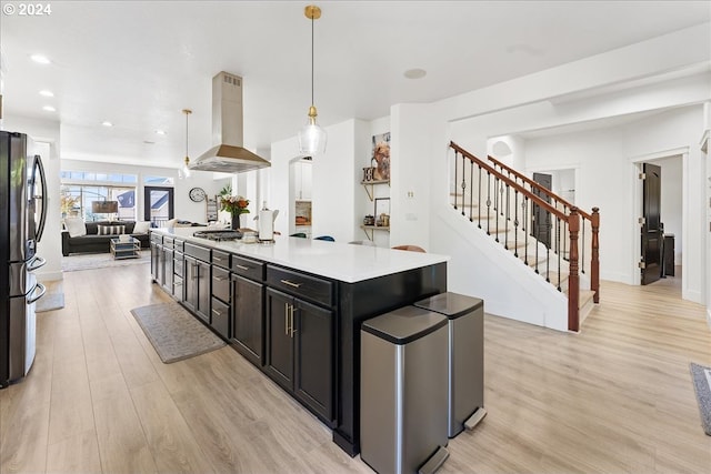 kitchen featuring light hardwood / wood-style floors, stainless steel appliances, exhaust hood, decorative light fixtures, and a kitchen island with sink