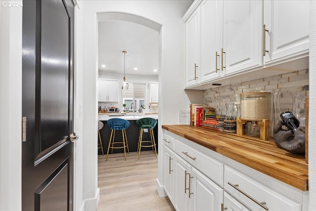 bar featuring light wood-type flooring, white cabinets, butcher block counters, backsplash, and decorative light fixtures