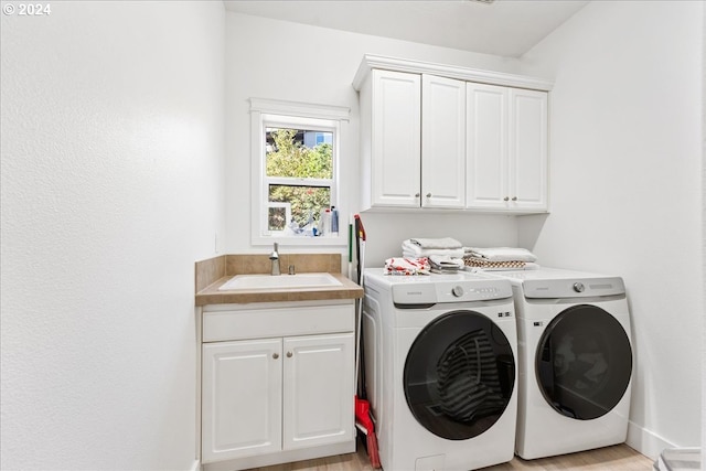 clothes washing area with cabinets, washing machine and dryer, light hardwood / wood-style flooring, and sink