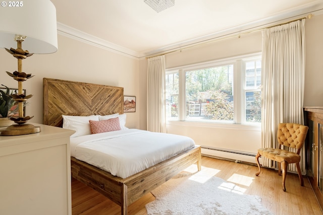 bedroom with crown molding, light hardwood / wood-style floors, and baseboard heating